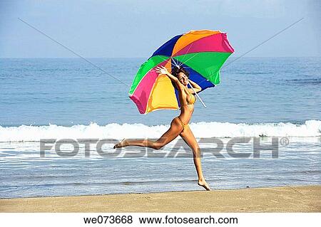 Stock Photo - Latin girl jumping on the beach with an umbrella. Fotosearch
