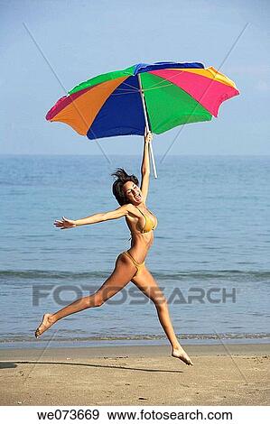 Stock Photo - Latin girl jumping on the beach with an umbrella. Fotosearch