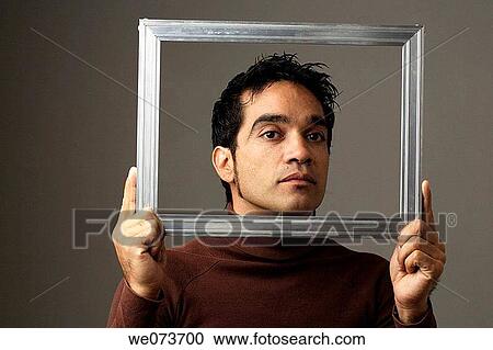 Stock Image - Latin man poses behind a picture frame. Fotosearch