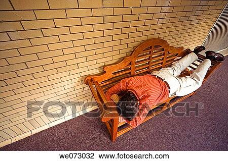 Man lying on a wood bench in the lobby of an office building View Large Photo Image Stock Image - Man lying on a wood bench in the lobby of an office building. Fotosearch