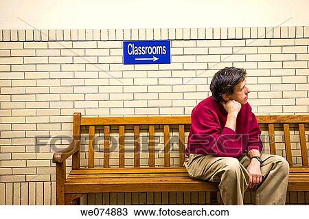 Man sitting on a bench in a college classroom building with a sign above it reading? Classrooms? and a directional arrow. View Large Photo Image Stock Image - Man sitting on a bench in a college classroom building with a sign above it reading? Classrooms? and a directional arrow.. Fotosearch