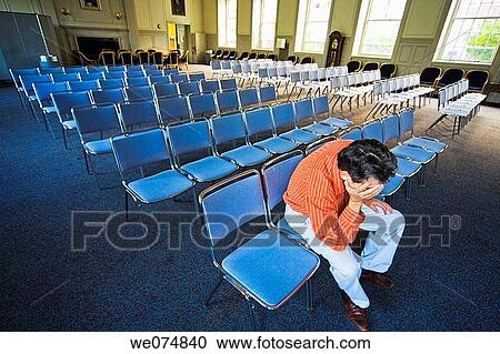 Stock Image - Man sitting on a chair in an otherwise empty auditorium.. Fotosearch