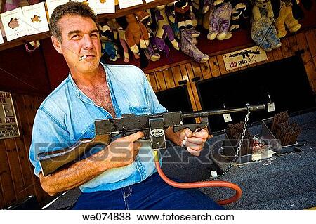Middle-age man, smoking a cigarette, holding a machine gun at a carnival booth. View Large Photo Image Stock Photo - Middle-age man, smoking a cigarette, holding a machine gun at a carnival booth.. Fotosearch
