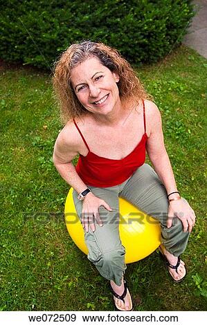 Stock Photo - Middle age woman sitting on a large rubber ball outside on the grass. Fotosearch