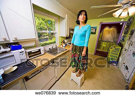 Middle_age woman standing on a stool in her kitchen. View Large Photo Image Stock Photo - Middle_age woman standing on a stool in her kitchen.. Fotosearch
