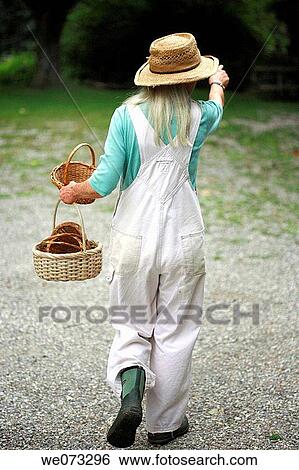 Senior woman with straw hat walking with baskets in hand from back pointing View Large Photo Image Stock Photograph - Senior woman with straw hat walking with baskets in hand from back pointing. Fotosearch