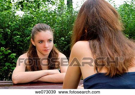 Teen sisters sitting and talking together at a picnic table, the older sister's back is to the camera. View Large Photo Image Stock Photo - Teen sisters sitting and talking together at a picnic table, the older sister's back is to the camera.. Fotosearch