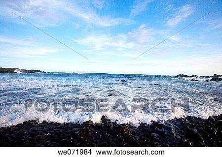 Picture - The Pacific Ocean washes ashore over small rocks near South Point on the Big Island, Hawaii in Hawaii, USA. South Point is the southern most point of the United States.. Fotosearch