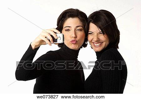 Twin sisters having their picture taken with a cell phone. One smiling, the other one blowing a kiss View Large Photo Image Stock Photo - Twin sisters having their picture taken with a cell phone. One smiling, the other one blowing a kiss. Fotosearch