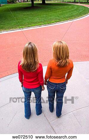 Two young blond women, who are sisters, with their backs to the camera, standing together in front of a brick path View Large Photo Image Stock Image - Two young blond women, who are sisters, with their backs to the camera, standing together in front of a brick path. Fotosearch