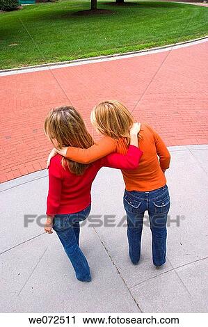 Two young blond women, who are sisters, with their backs to the camera, clowning together in front of a brick path View Large Photo Image Stock Image - Two young blond women, who are sisters, with their backs to the camera, clowning together in front of a brick path. Fotosearch