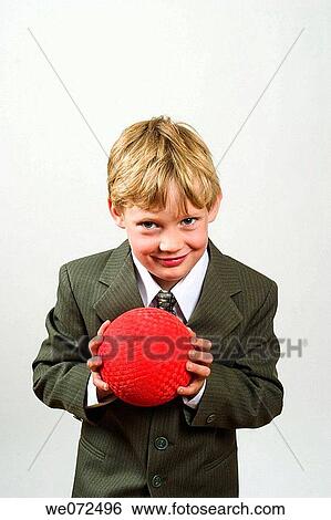 Stock Photograph - Young blond boy, wearing a suit, holding a rubber ball in his hands.. Fotosearch
