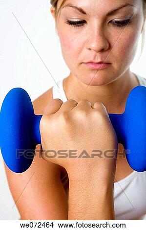 Young blond woman focuses on lifting weight during her exercise. View Large Photo Image Picture - Young blond woman focuses on lifting weight during her exercise.. Fotosearch