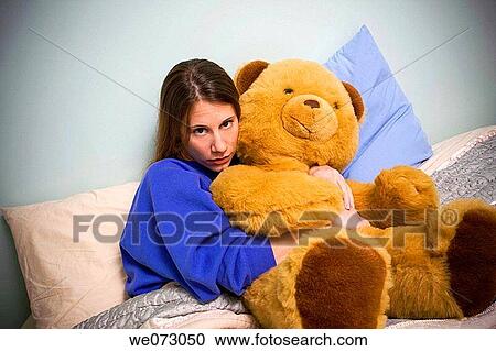Young woman sitting on her bed, holding a very large stuffed animal. View Large Photo Image Stock Image - Young woman sitting on her bed, holding a very large stuffed animal.. Fotosearch