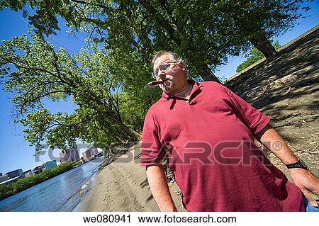 Middle-age man standing by a river, smoking a cigar. View Large Photo Image Stock Image - Middle-age man standing by a river, smoking a cigar.. Fotosearch