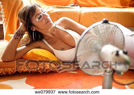 Stock Photo - Woman in her late 30s relaxing at home in front of a fan. Fotosearch