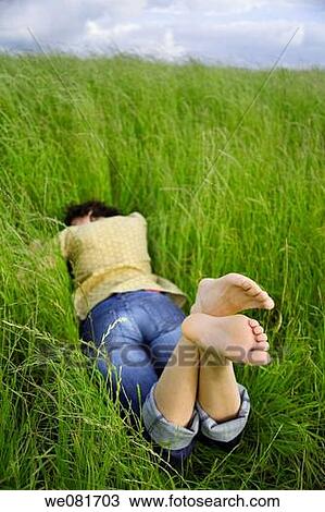 Stock Image - Young barefooted woman resting on a peaceful field of grass. Fotosearch