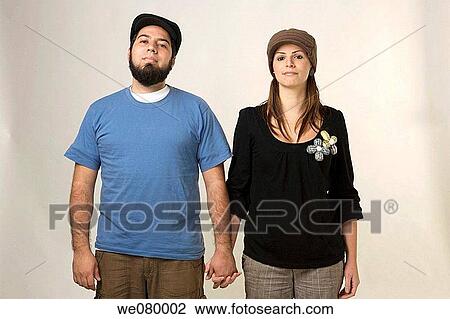 Young trendy couple holding hands looking at the camera View Large Photo Image Stock Image - Young trendy couple holding hands looking at the camera. Fotosearch