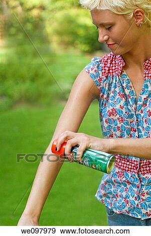 Stock Photo - 21 year old blond woman in a summer garden spraying insect repellant on her arm. Fotosearch