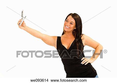A beautiful young female caucasian wearing an casual outfit and using a cell phone to take a picture of herself She is on a white background View Large Photo Image Picture - A beautiful young female caucasian wearing an casual outfit and using a cell phone to take a picture of herself She is on a white background. Fotosearch