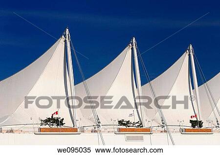 Stock Photography - Abstract white Canada Place sails in Vancouver against a blue sky with Canadian flags. Fotosearch