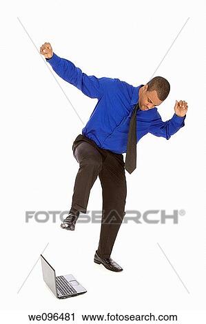 Stock Image - African American businessman kicking a laptop on white background. Fotosearch