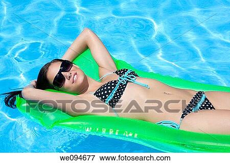 Attractive slim and tanned young lady lying on inflatable sunbed on sunny swimming pool on vacation or holiday View Large Photo Image Stock Photo - Attractive slim and tanned young lady lying on inflatable sunbed on sunny swimming pool on vacation or holiday. Fotosearch