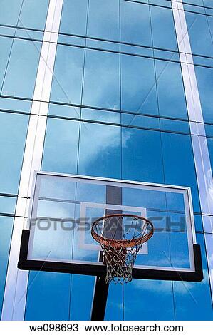 Stock Image - Basketball hoop with glass backboard in front of sleek glass modern office building reflecting clouds in the surface. San Mateo, California, USA.. Fotosearch