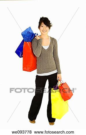 Beautiful Asian teen holding shopping bags while standing on a white background View Large Photo Image Stock Photo - Beautiful Asian teen holding shopping bags while standing on a white background. Fotosearch
