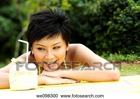 Stock Image - Beautiful asian woman looking at coconut. Fotosearch