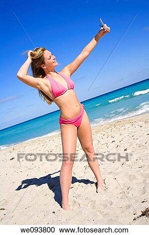Beautiful Caucasian female teenage standing on the beach and using a cell phone to take a picture of herself She is wearing a colorful pink bikini View Large Photo Image Stock Image - Beautiful Caucasian female teenage standing on the beach and using a cell phone to take a picture of herself She is wearing a colorful pink bikini. Fotosearch