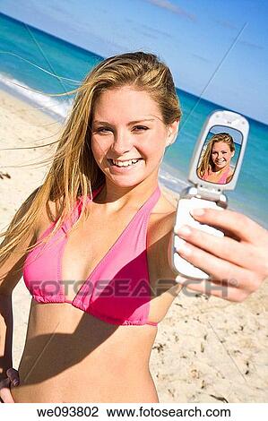 Beautiful Caucasian female teenage standing on the beach and using a cell phone to take a picture of herself She is wearing a colorful pink bikini View Large Photo Image Stock Image - Beautiful Caucasian female teenage standing on the beach and using a cell phone to take a picture of herself She is wearing a colorful pink bikini. Fotosearch