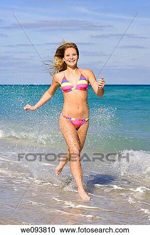 Beautiful Caucasian female teenage running through to surf wearing a colorful bikini View Large Photo Image Stock Image - Beautiful Caucasian female teenage running through to surf wearing a colorful bikini. Fotosearch
