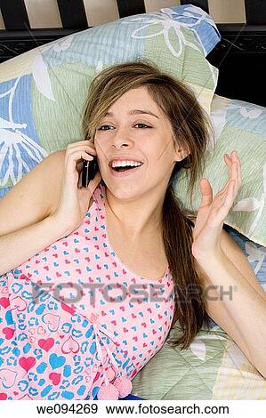 Beautiful Caucasian female teenager laying in bed talking with friends in a cell phone View Large Photo Image Stock Photo - Beautiful Caucasian female teenager laying in bed talking with friends in a cell phone. Fotosearch