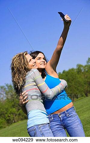 Beautiful Caucasian female teenages standing in a park and using a cell phone to take a picture View Large Photo Image Stock Photo - Beautiful Caucasian female teenages standing in a park and using a cell phone to take a picture. Fotosearch