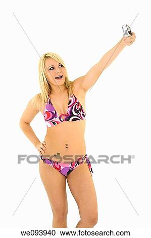 Stock Image - Beautiful Caucasian woman in a bikini using a camera to take a picture of herself. Fotosearch