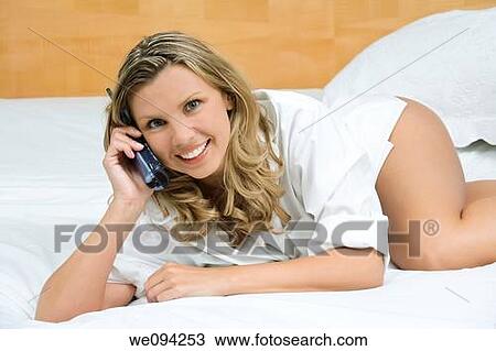 Stock Image - Beautiful caucasian woman laying in bed talking on the phone. Fotosearch