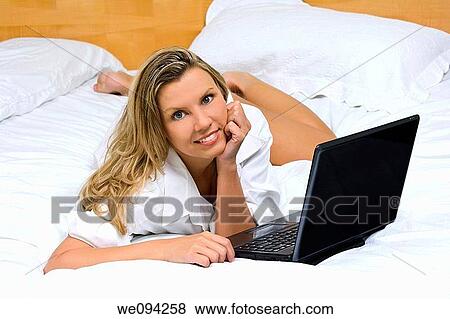 Beautiful caucasian woman laying in bed working on a laptop computer View Large Photo Image Stock Photo - Beautiful caucasian woman laying in bed working on a laptop computer. Fotosearch
