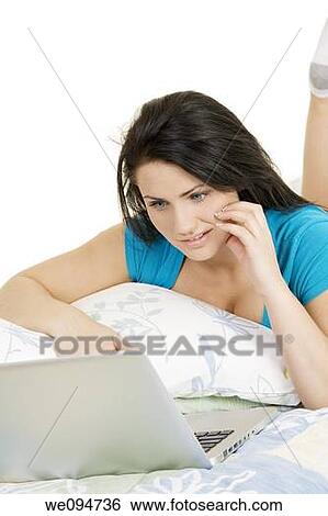Stock Photograph - Beautiful Caucasian woman laying in bed working on laptop computer. Fotosearch