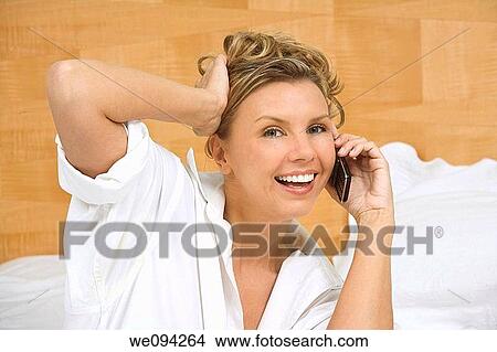Picture - Beautiful caucasian woman setting in bed talking on the phone. Fotosearch