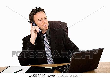 Caucasian businessman setting a desk talking on the phone View Large Photo Image Picture - Caucasian businessman setting a desk talking on the phone. Fotosearch