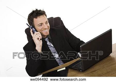 Caucasian businessman setting at a desk talking on the phone and smiling while working on a laptop View Large Photo Image Stock Image - Caucasian businessman setting at a desk talking on the phone and smiling while working on a laptop. Fotosearch