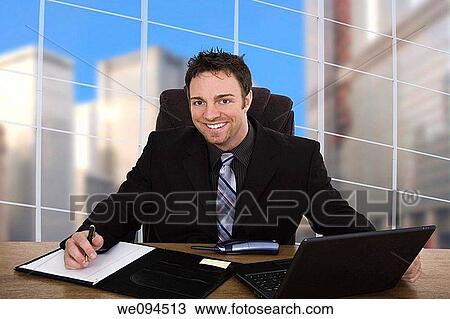 Stock Image - Caucasian businessman setting at a desk and smiling. Fotosearch