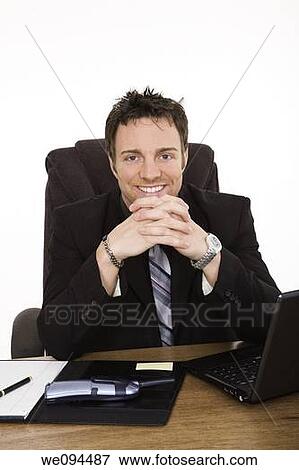 Caucasian businessman setting at a desk talking and smiling View Large Photo Image Stock Photo - Caucasian businessman setting at a desk talking and smiling. Fotosearch