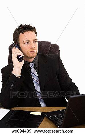 Stock Photo - Caucasian businessman setting at a desk talking on the phone. Fotosearch