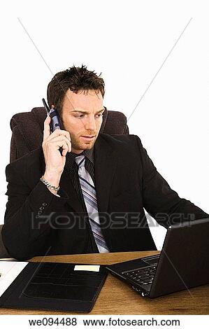 Caucasian businessman sitting at a desk while talking on the telephone View Large Photo Image Stock Photo - Caucasian businessman sitting at a desk while talking on the telephone. Fotosearch