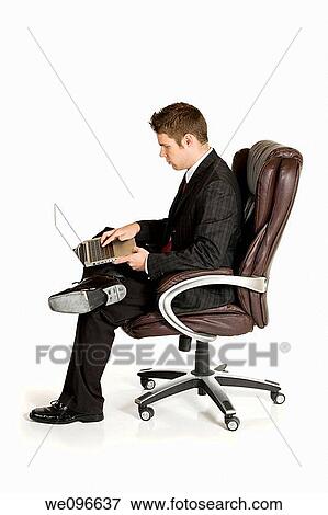 Caucasian businessman sitting in a chair working on a laptop View Large Photo Image Stock Photo - Caucasian businessman sitting in a chair working on a laptop. Fotosearch