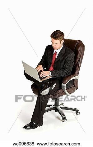 Caucasian businessman sitting in a chair working on a laptop View Large Photo Image Stock Photo - Caucasian businessman sitting in a chair working on a laptop. Fotosearch