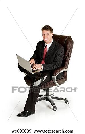 Caucasian businessman sitting in a chair working on a laptop View Large Photo Image Stock Photo - Caucasian businessman sitting in a chair working on a laptop. Fotosearch