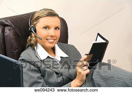 Stock Image - Caucasian businesswoman in her early 30s setting at a desk going over a day planner. Fotosearch